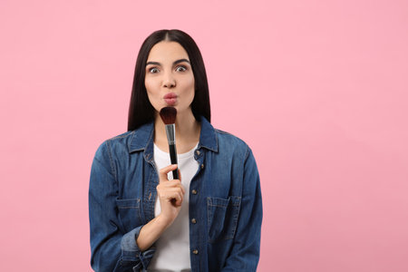 Emotional woman with makeup brush on pink background. Space for textの写真素材