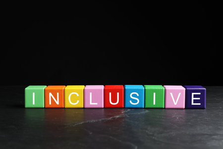 Colorful cubes with word Inclusive on marble table against black background. Space for textの写真素材