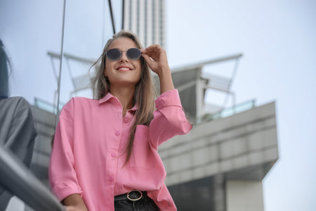 Beautiful young woman in stylish sunglasses near building outdoors, space for textの写真素材