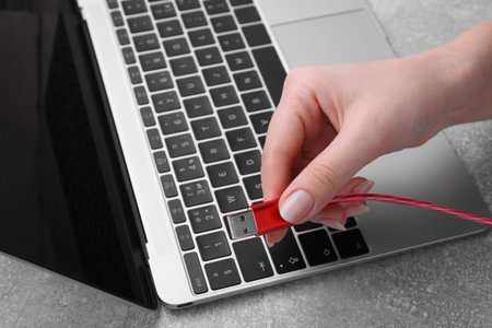 Woman holding USB cable near laptop at gray table, closeup