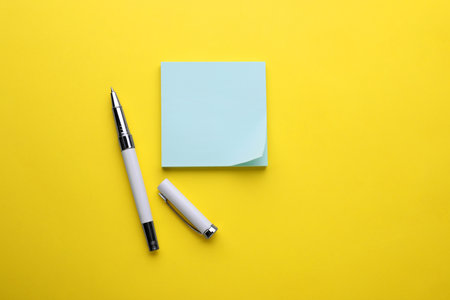 Paper note and pen on yellow background, flat lay. Space for text