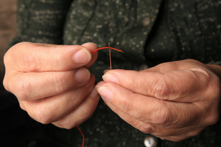 Closeup view of woman threading needle indoors. Sewing equipment