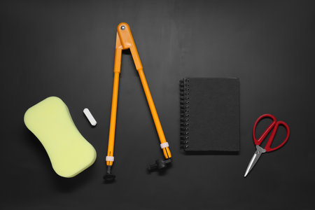 Compass, sponge, chalk, notebook and scissors on black table, flat lay