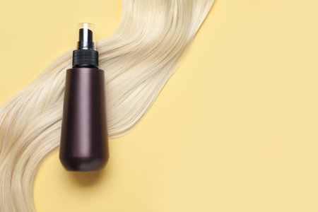 Spray bottle with thermal protection and lock of blonde hair on yellow background, flat lay. Space for textの写真素材