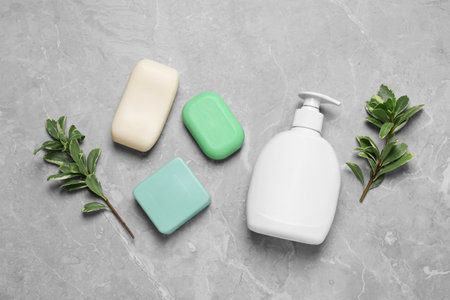 Different soap bars, dispenser and green plants on light gray table, flat lay