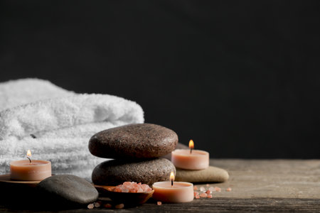 Beautiful composition with spa stones and burning candles on wooden table against black background. Space for textの写真素材