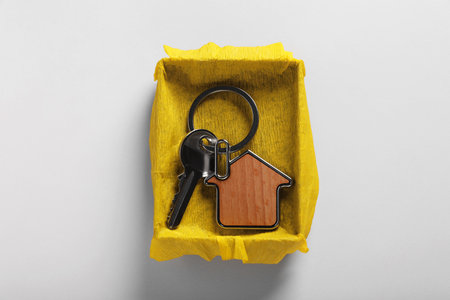 Key with trinket in shape of house and gift box on light gray background, top view. house warming partyの写真素材