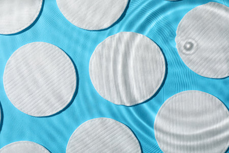 Many cotton pads in water on light blue background, flat lay