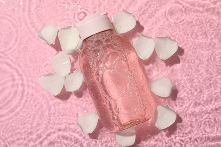 Wet bottle of micellar water and petals on pink background, top viewの写真素材