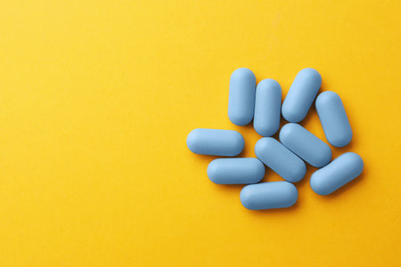 Pills and space for text on orange background, top view. Potency problem