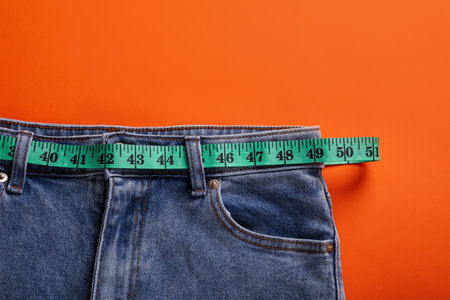 Jeans and measuring tape on orange background, top view. weight loss conceptの写真素材