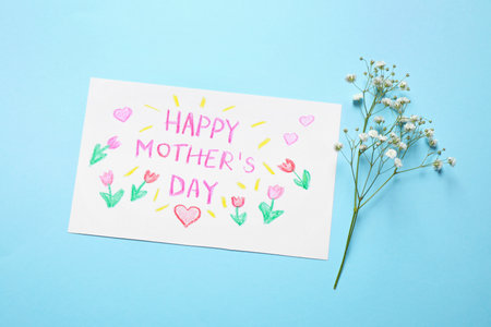 Handmade greeting card for Mother's day and flower on light blue background, flat lay