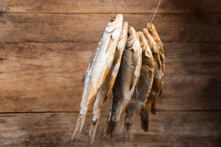 Dried fish hanging on rope against wooden background