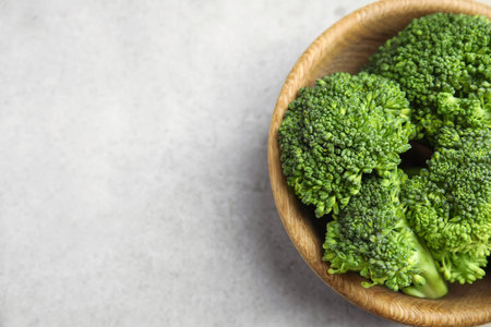 Fresh green broccoli in bowl on light table, top view. Space for text