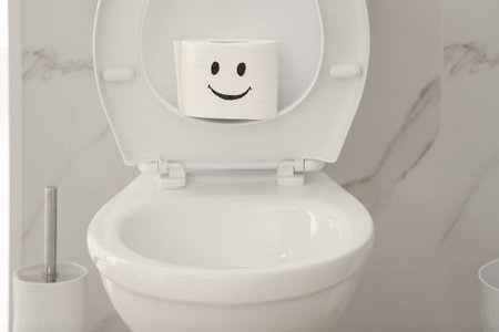 Roll of paper with funny face on toilet bowl in bathroom