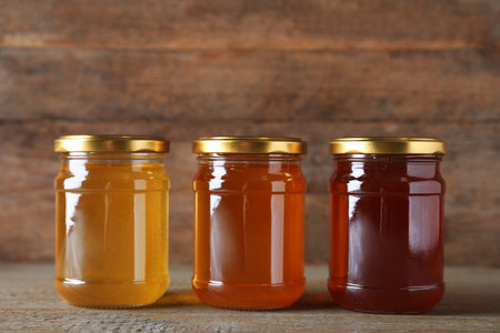 Jars with different types of organic honey on wooden tableの写真素材