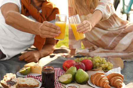 Young couple having picnic outdoors, focus on hands with glasses of juiceの写真素材