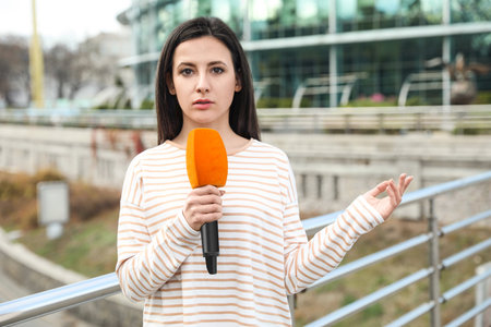 Young female journalist with microphone working on city streetの写真素材
