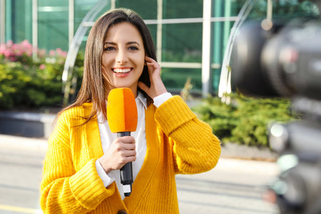 Young female journalist with microphone working on city streetの写真素材