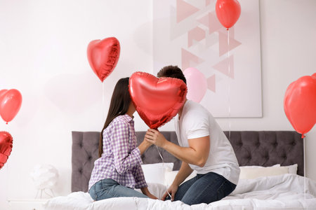 Romantic couple hiding behind heart shaped balloon in bedroom. Valentine's day celebrationの写真素材