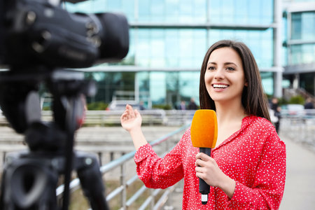 Young female journalist with microphone working on city streetの写真素材