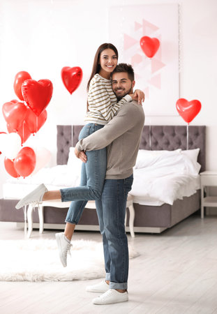 Lovely young couple in bedroom decorated with heart shaped balloons. Valentine's day celebrationの写真素材