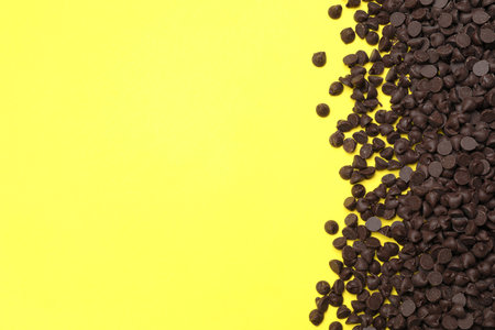 Pile of delicious dark chocolate chips on yellow background, top view. Space for textの写真素材