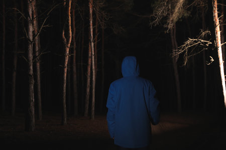 Man with bright flashlight in the forest at night