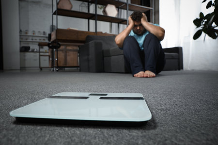 Scales and depressed overweight man on floor at homeの写真素材