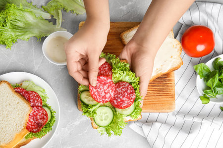 Woman making tasty sandwich at light gray marble table, top viewの写真素材