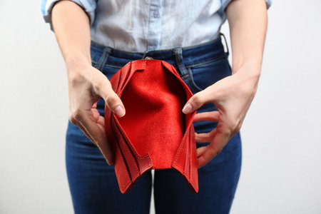 Woman showing empty wallet on light background, closeup