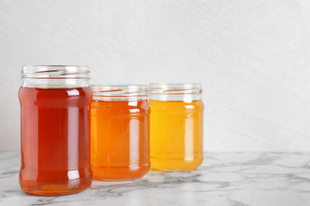 Jars with different types of organic honey on marble table against white backgroundの写真素材