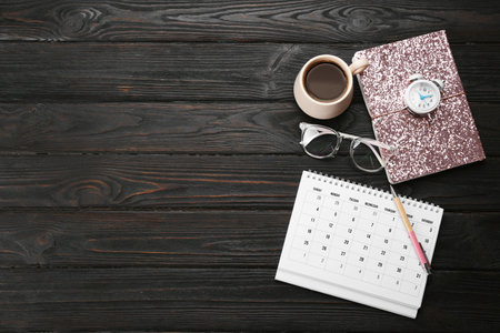 Flat lay composition with calendar and cup of coffee on black wooden table. Space for textの写真素材