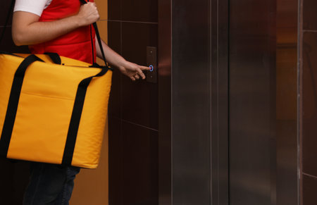 Male courier with thermo bag pushing elevator button, closeup. food delivery service