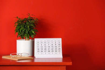 Paper calendar and plant on table near red wall. Space for textの写真素材