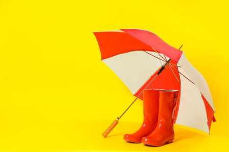 Colorful umbrella and red rubber boots on light yellow background. Space for textの写真素材