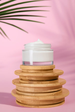 Open jar of cream on wooden display against pink backgroundの写真素材