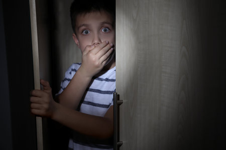 Scared little boy hiding in wardrobe. domestic violence conceptの写真素材