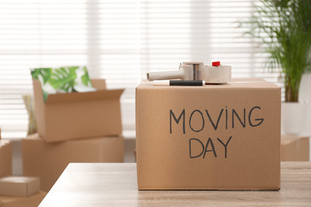 Cardboard box with words MOVING DAY and packaging items on wooden tableの写真素材