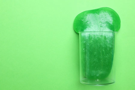 Overturned plastic container with bright slime on green background, top view. Space for textの写真素材