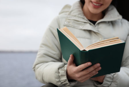 Woman reading book near river on cloudy day, closeupの写真素材