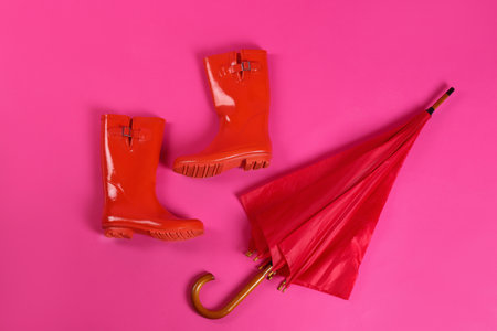 Beautiful red umbrella and rubber boots on pink background, flat layの写真素材