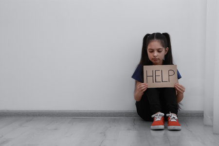 Sad little girl with sign HELP sitting on floor indoors, space for text. child in dangerの写真素材