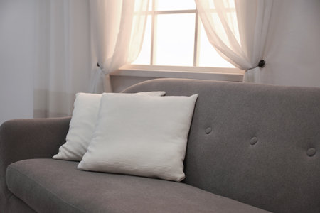 Modern comfortable sofa with pillows near window indoors. Stylish interiorの写真素材