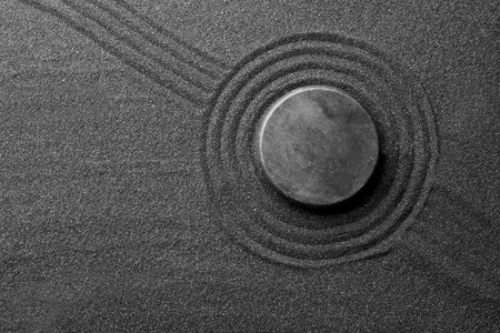 Zen garden stone on black sand with pattern, top view