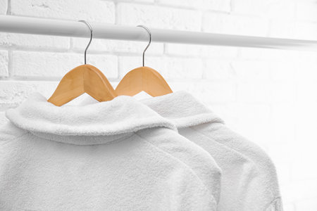 Fresh bathrobes hanging on rack near white brick wallの写真素材