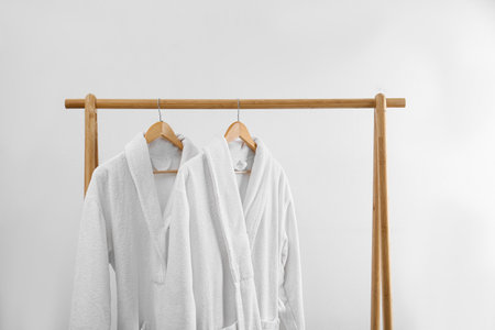 Fresh bathrobes hanging on rack near white wall