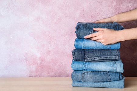 Woman folding stylish jeans on wooden table, closeup. Space for textの写真素材
