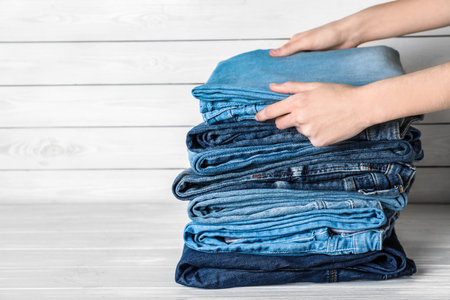Woman folding stylish jeans on white wooden table, closeup. Space for textの写真素材