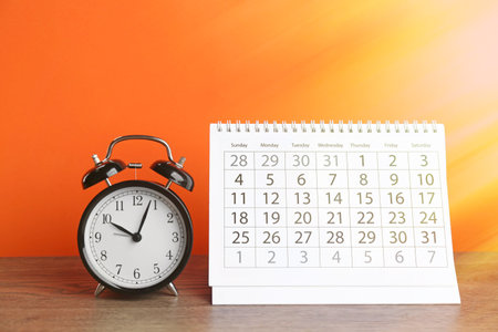 Calendar and alarm clock on wooden table against orange backgroundの写真素材